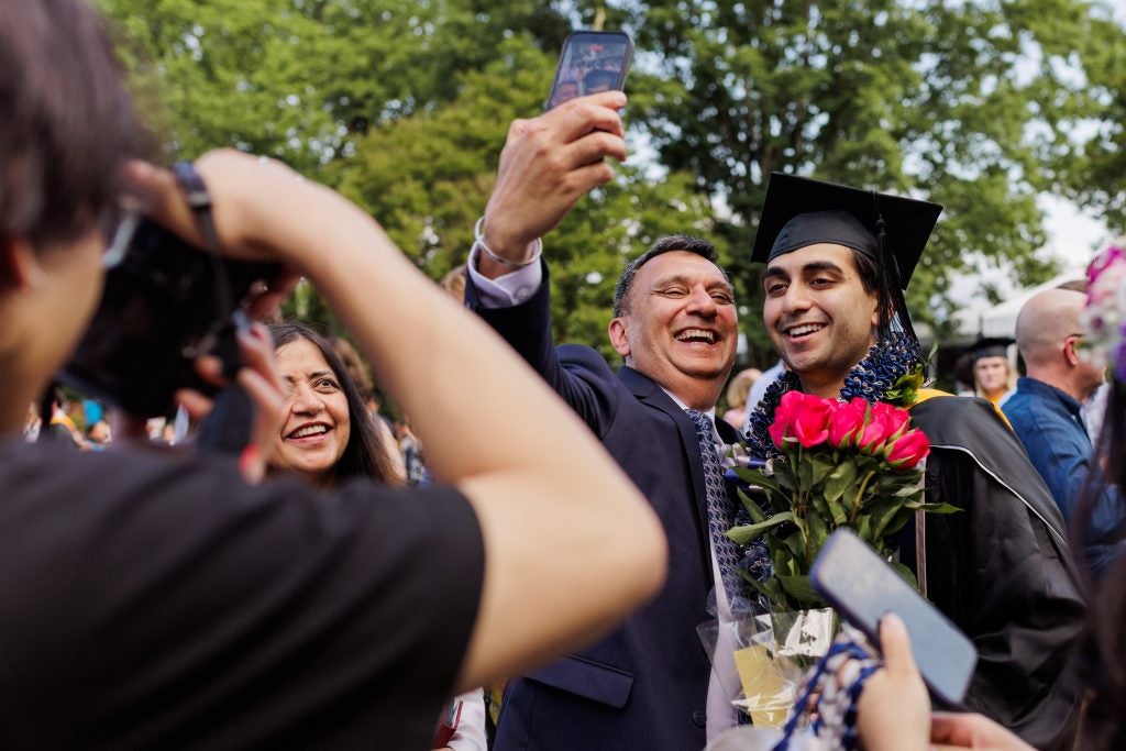 A father and son smile and take a selfie as the son holds flowers