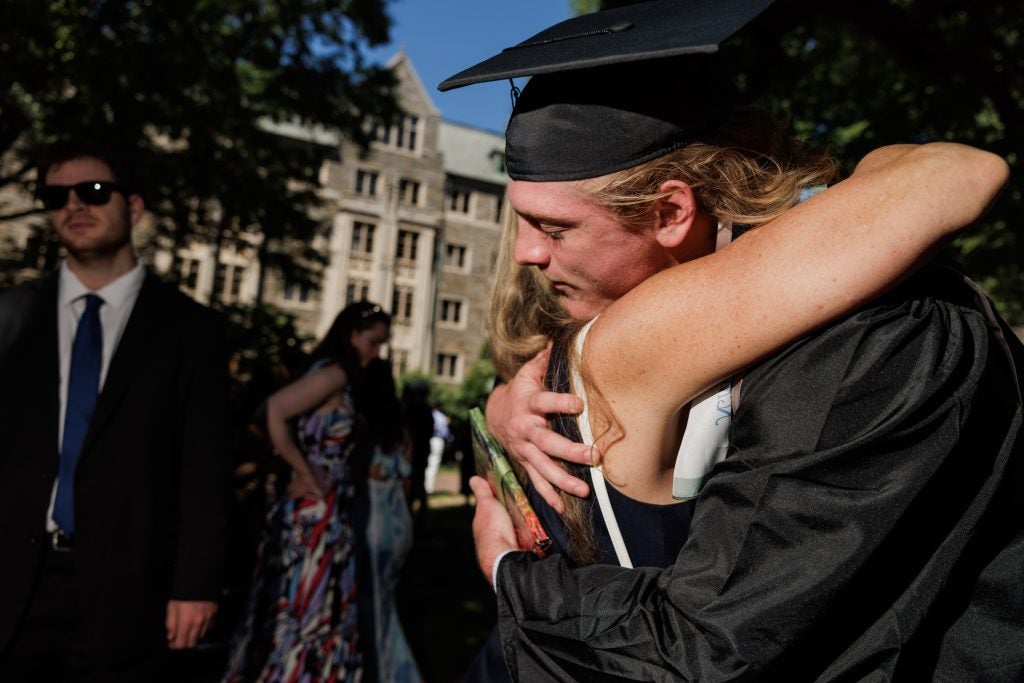 A male student in a cap and gown hugs a woman