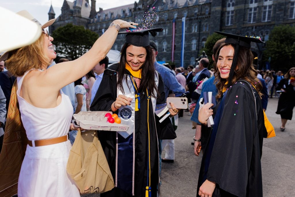 A woman drops confetti on a female students cap. Everyone laughs