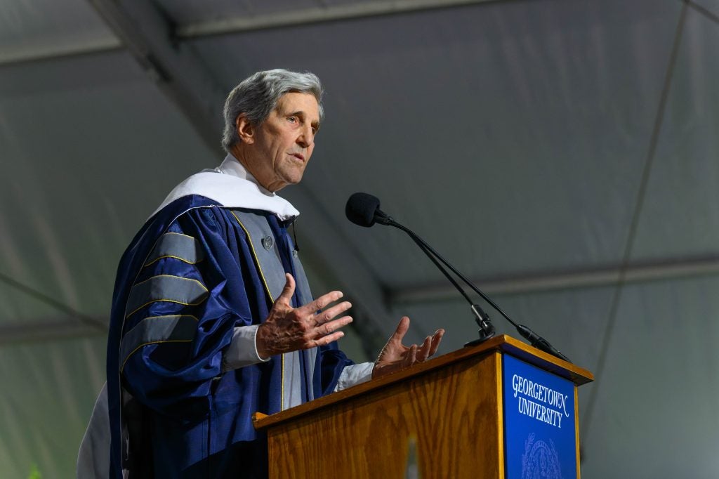 John Kerry speaks behind a podium in a graduation gown.