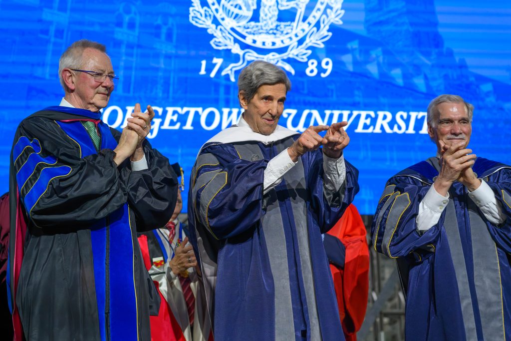 John Kerry in grad gown pointing to crowd on stage