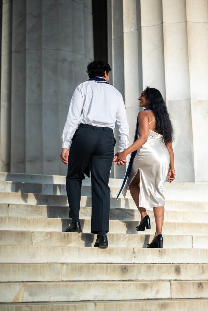 Two young people holding hands while going up stairs in graduation regalia