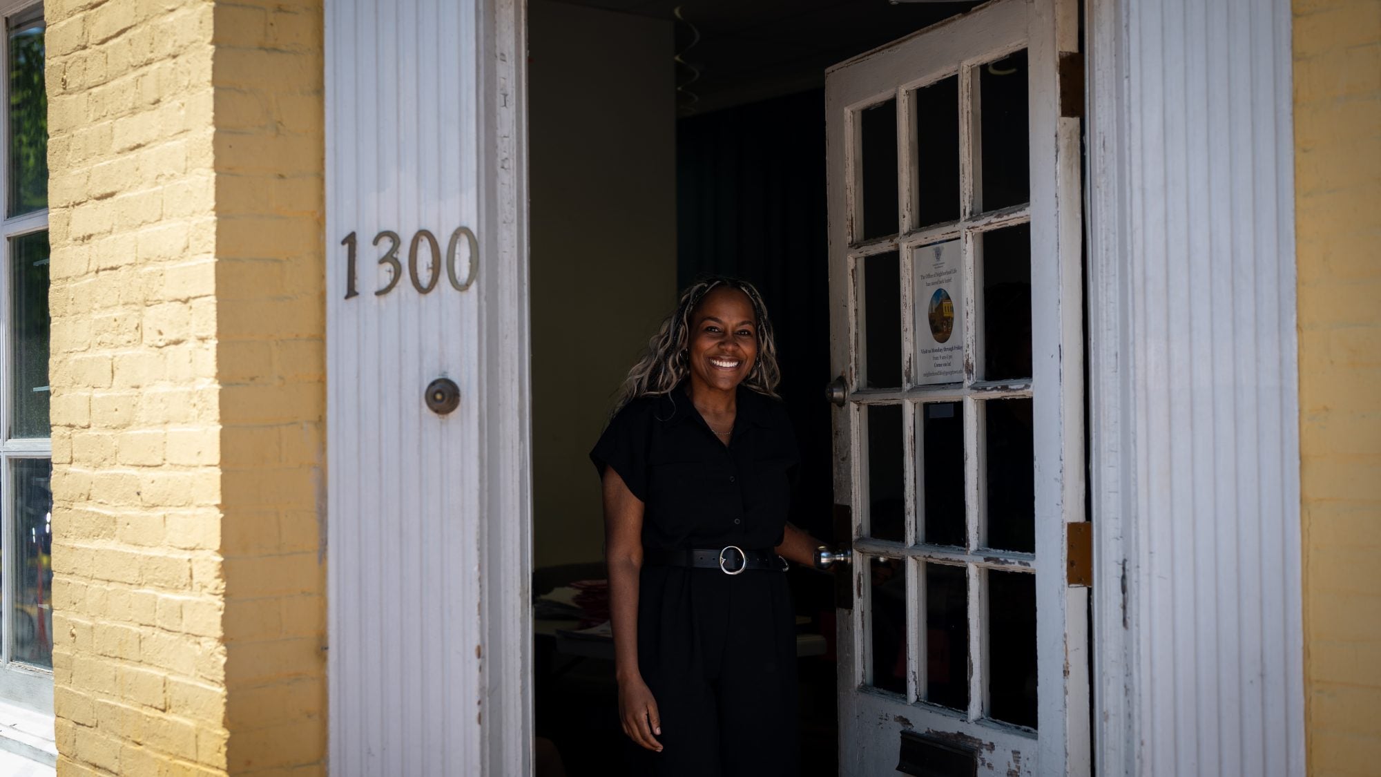 Black woman opening front door of a yellow building while smiling