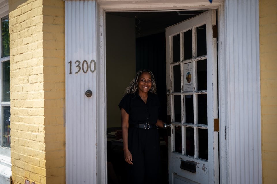 Black woman opening front door of a yellow building while smiling