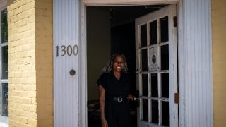 Black woman opening front door of a yellow building while smiling