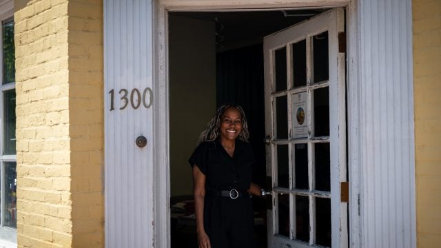 Black woman opening front door of a yellow building while smiling