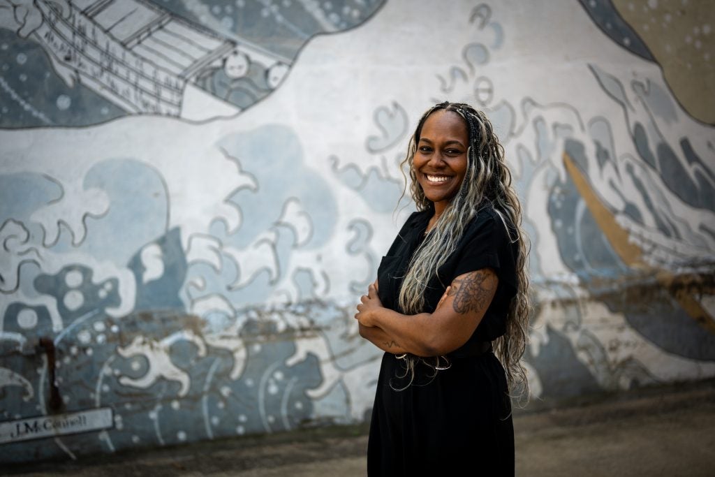 Black woman with arms crossed standing in front of a mural
