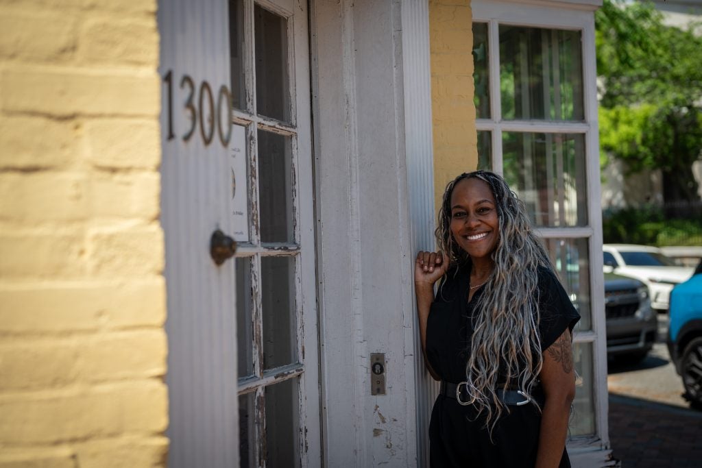 Black woman leaning against a yellow building while smiling