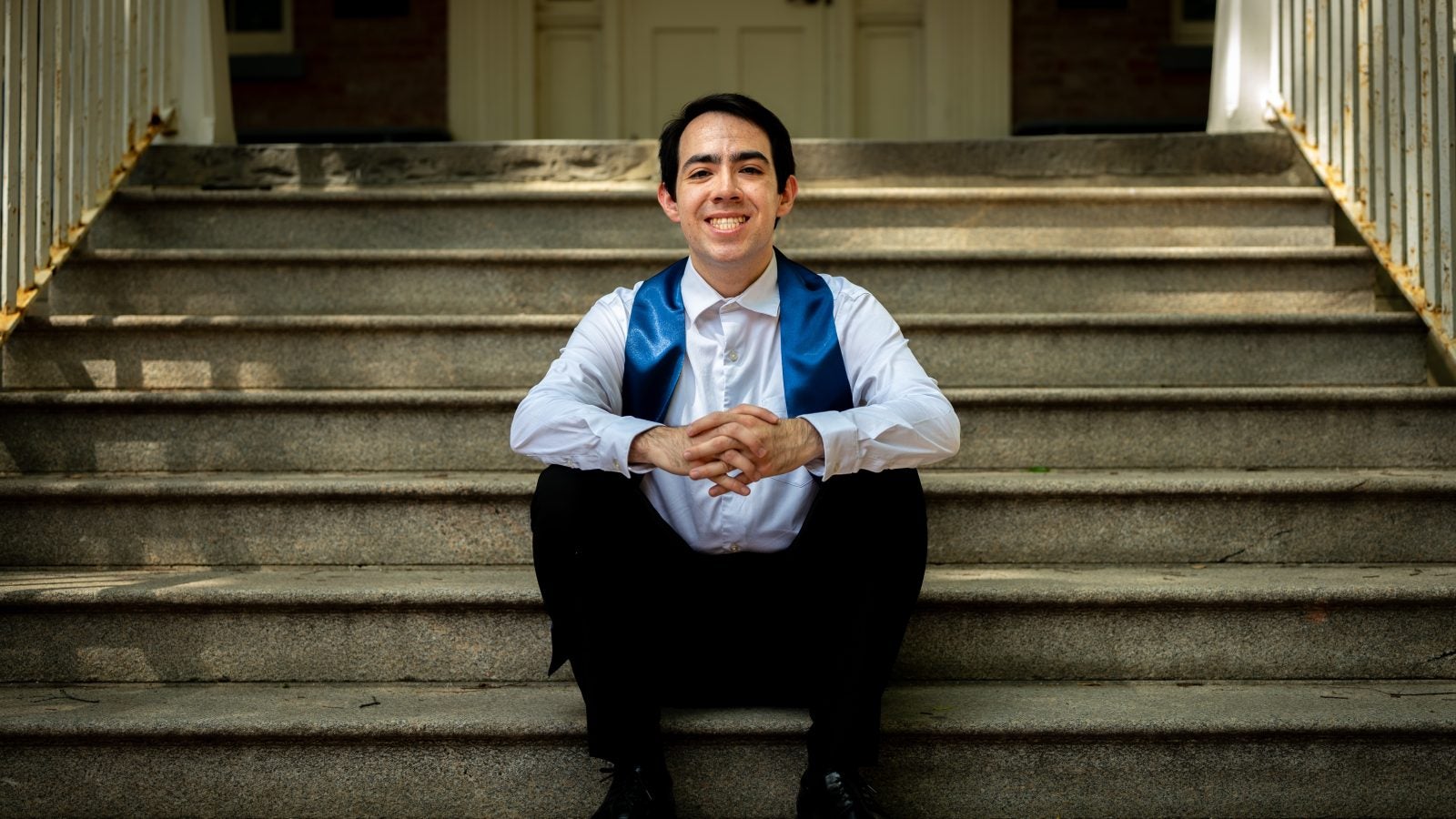 Young man in white shirt with a graduation stole sitting on steps