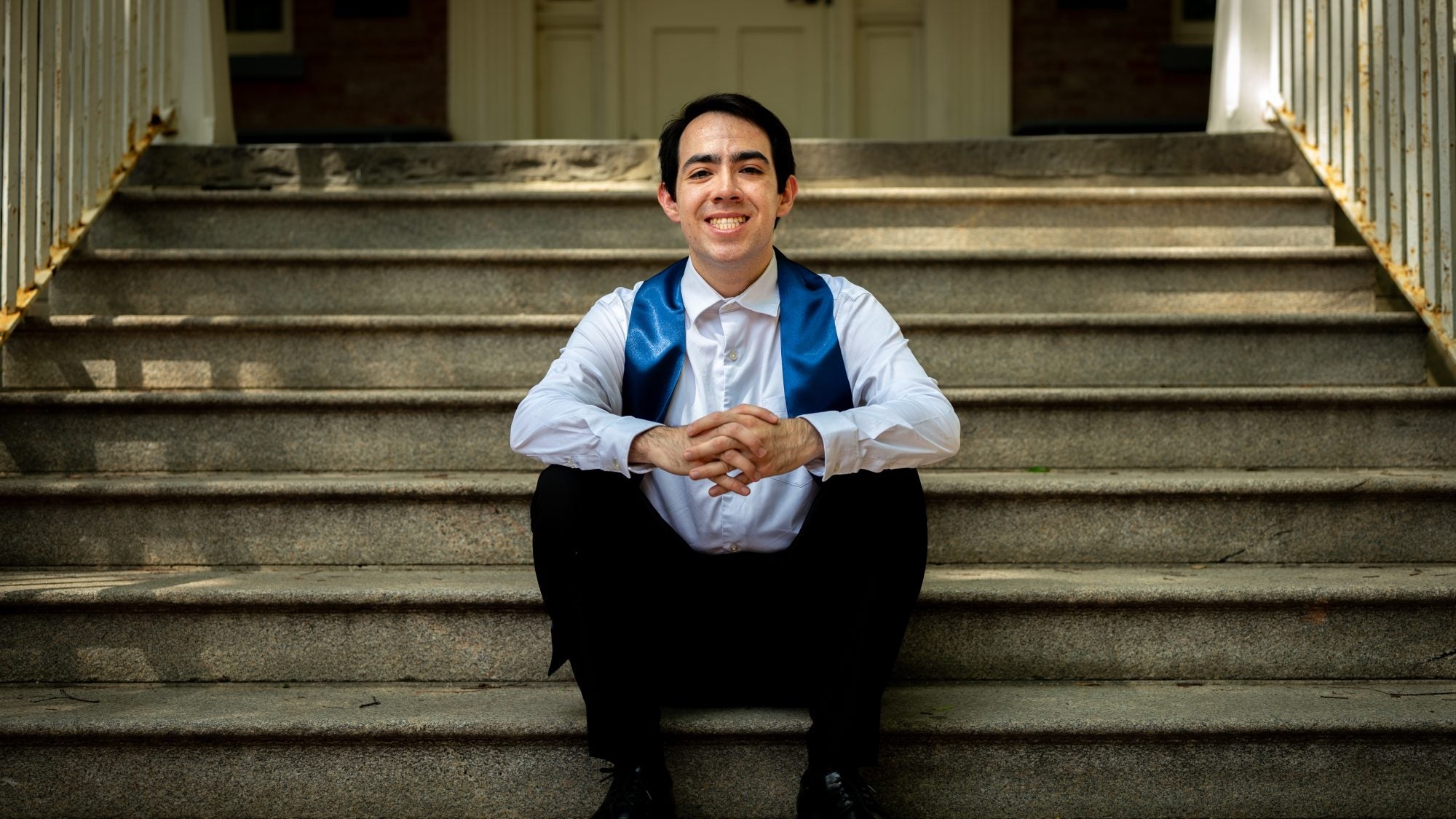 Young man in white shirt with a graduation stole sitting on steps