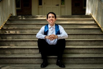 Young man in white shirt with a graduation stole sitting on steps