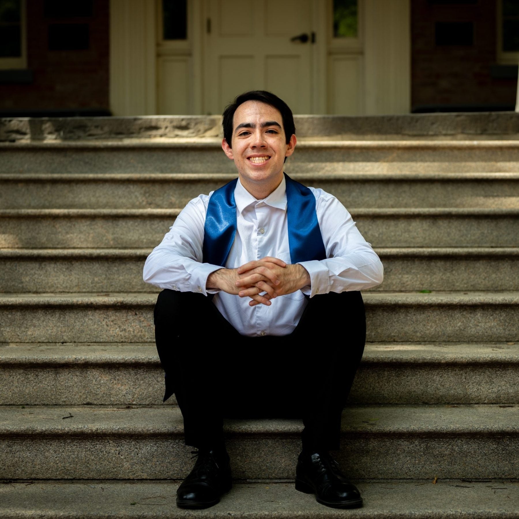 Young man in white shirt with a graduation stole sitting on steps