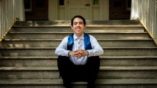 Young man in white shirt with a graduation stole sitting on steps