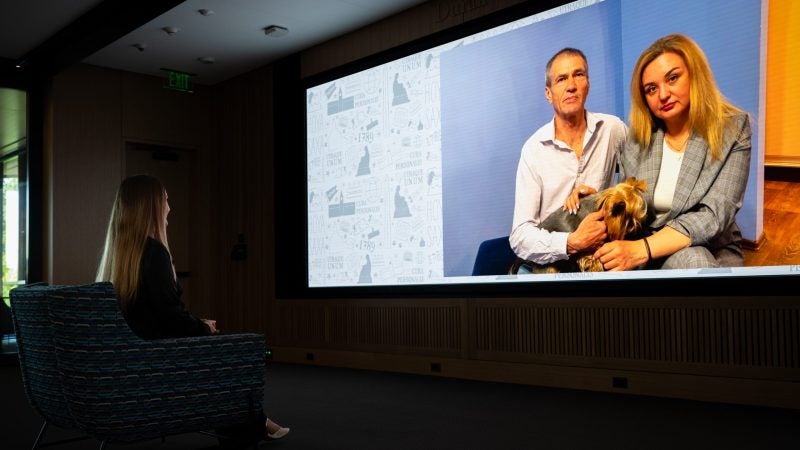 Young woman watches a big screen with her parents and dog on it