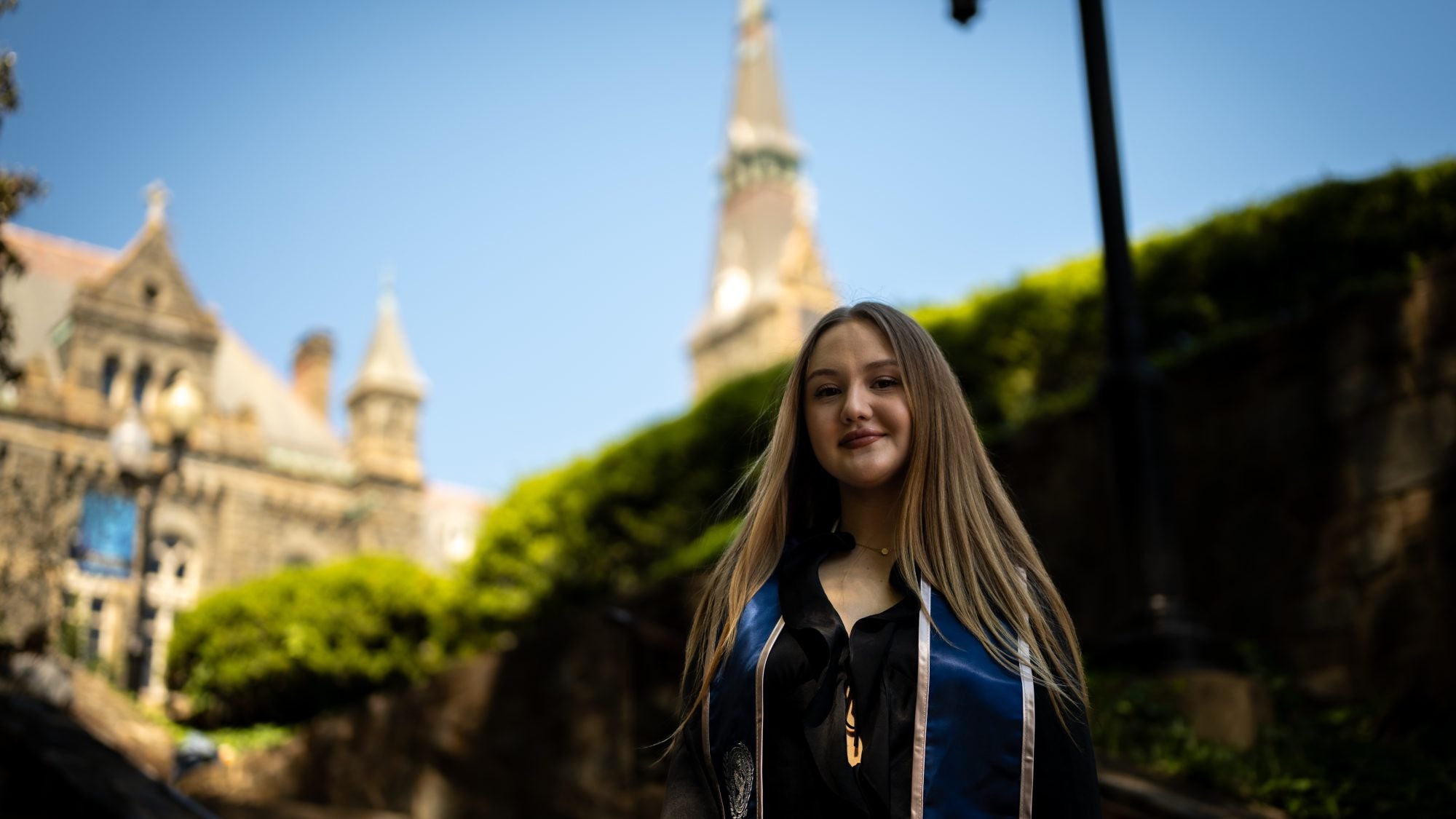 Young Caucasian woman in graduation regalia smiling with Healy Hall in the background
