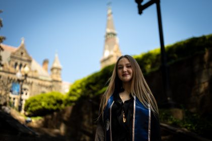 Young Caucasian woman in graduation regalia smiling with Healy Hall in the background