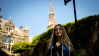 Young Caucasian woman in graduation regalia smiling with Healy Hall in the background