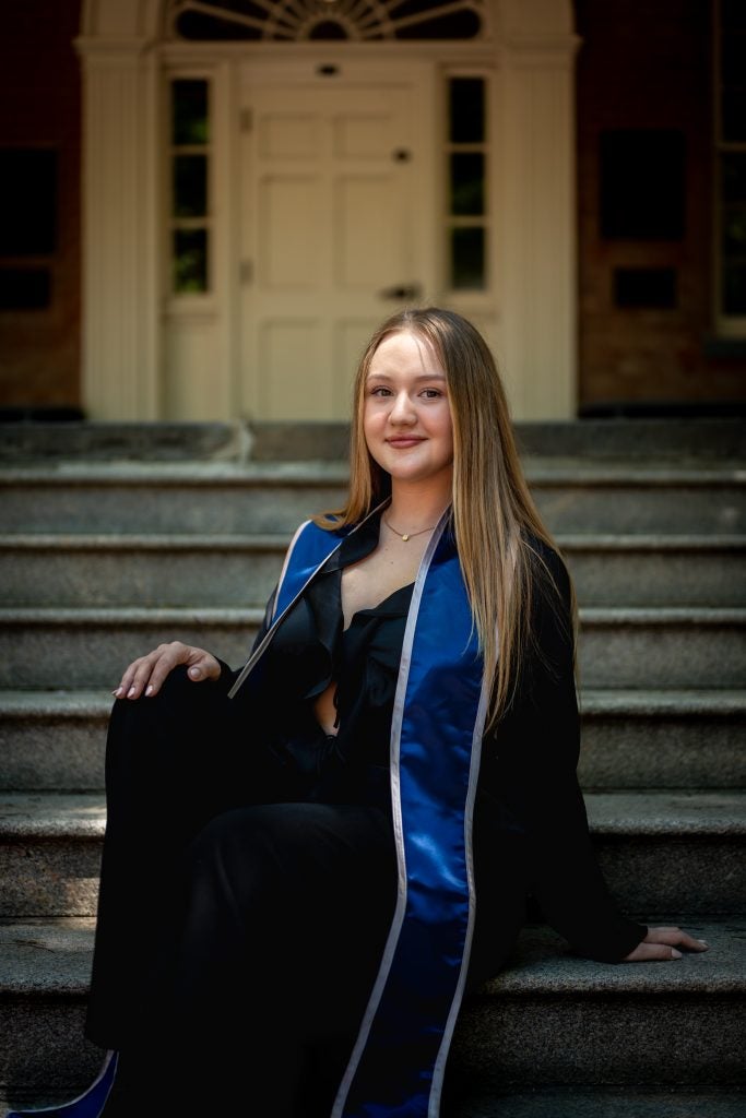 Young Caucasian woman in graduation regalia smiling while sitting on steps