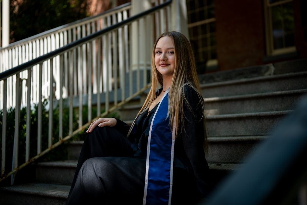 Young Caucasian woman in graduation regalia smiling and sitting on steps