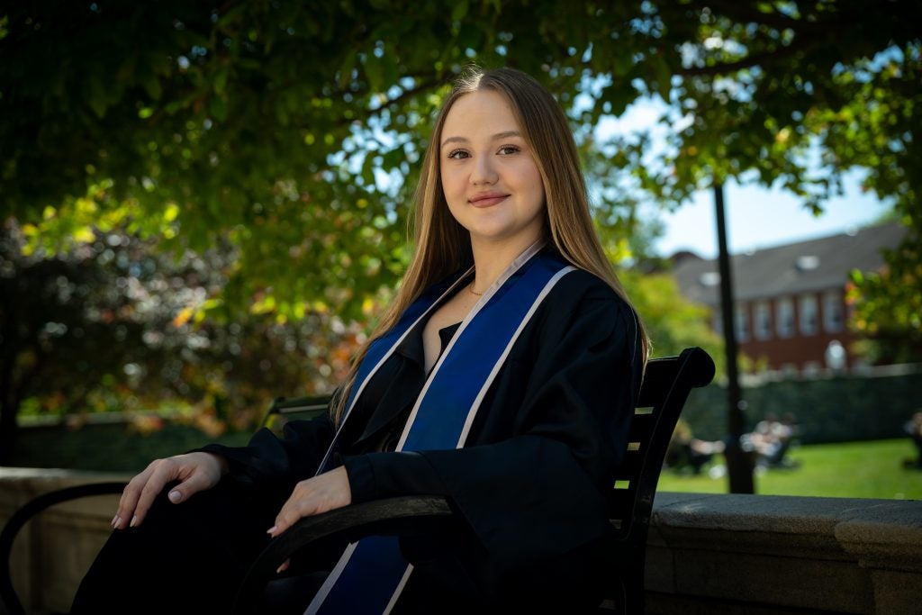 Young Caucasian woman in graduation regalia smiling sitting on a bench