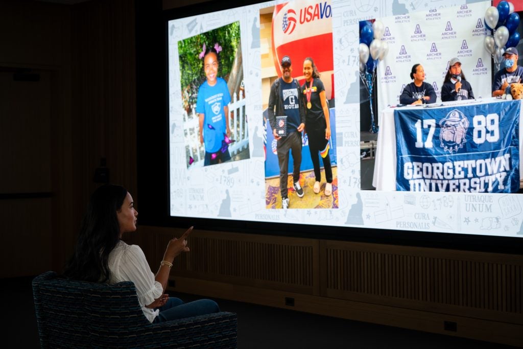 Young woman points to a big screen of photos from throughout her childhood