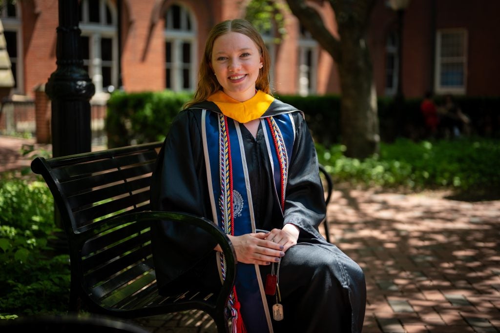 Young Caucasian woman smiling in grad regalia sitting on a bench