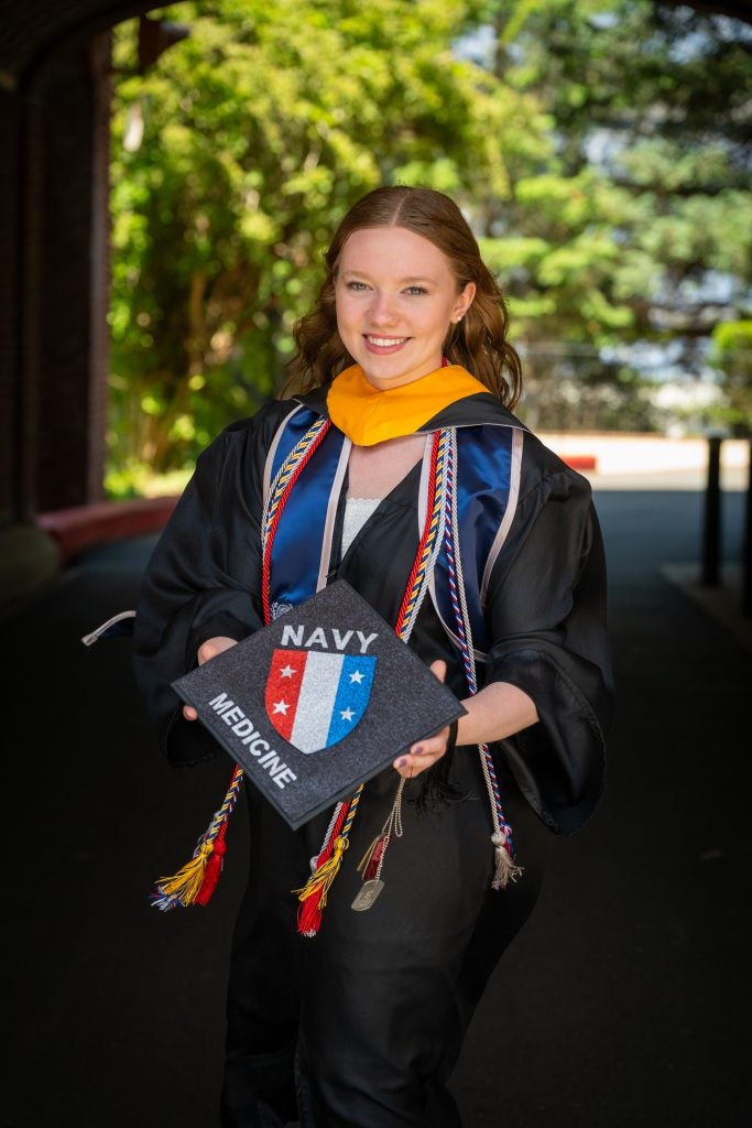 Young Caucasian woman smiling in grad regalia holding a grad cap