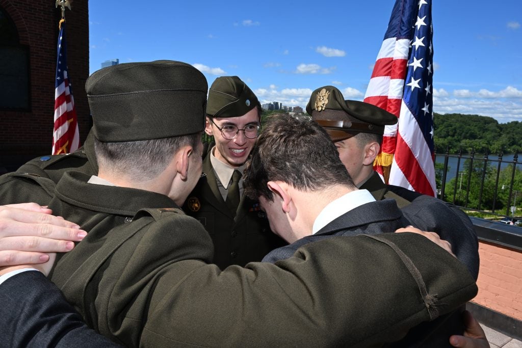 A group of students dressed in military uniforms huddle together and smile