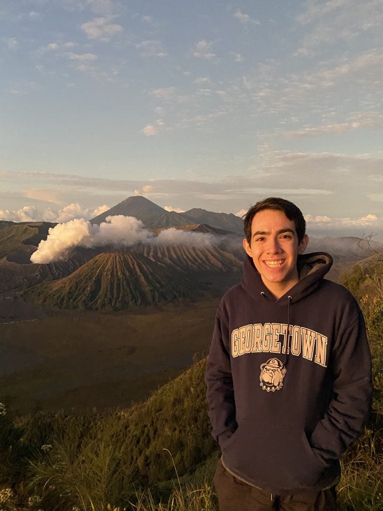 Young man in GU sweatshirt with a volcano behind him around sunrise