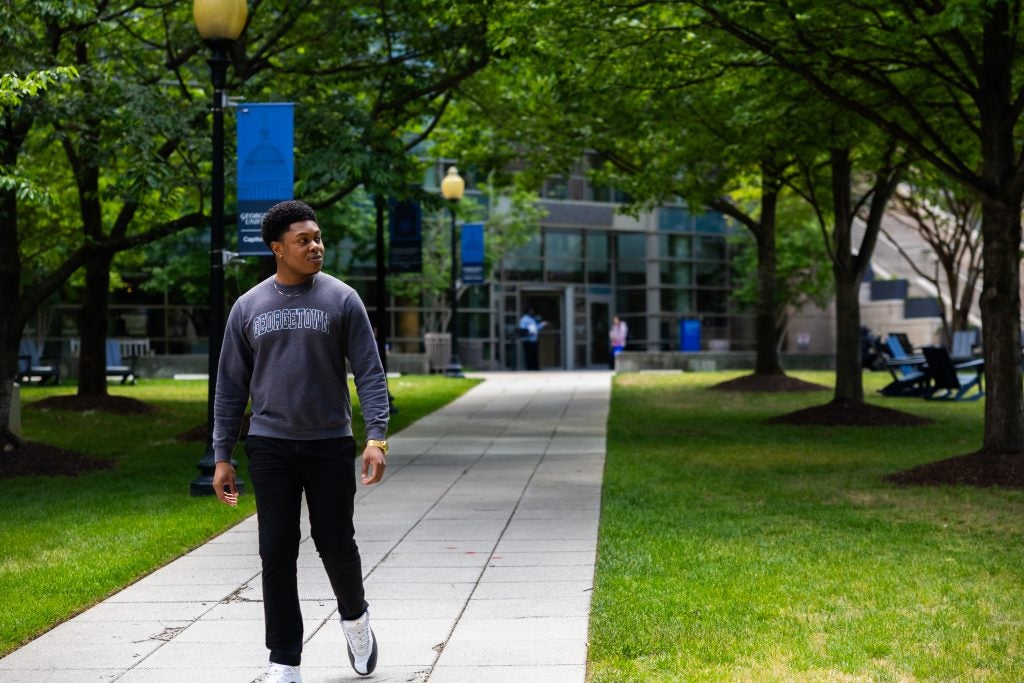 A young man walks on a sidewalk on Georgetown Law's campus