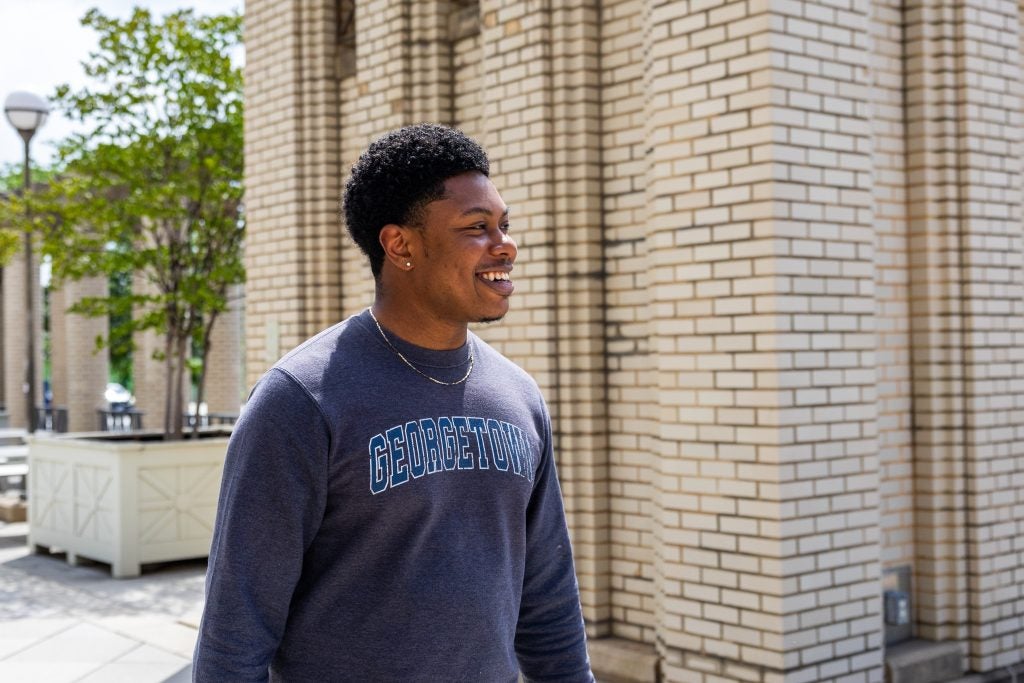 A young man smiles while wearing a Georgetown long-sleeve shirt and walking outside