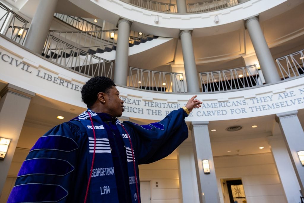 A graduating law student in a purple graduation gown points up at a circular lobby