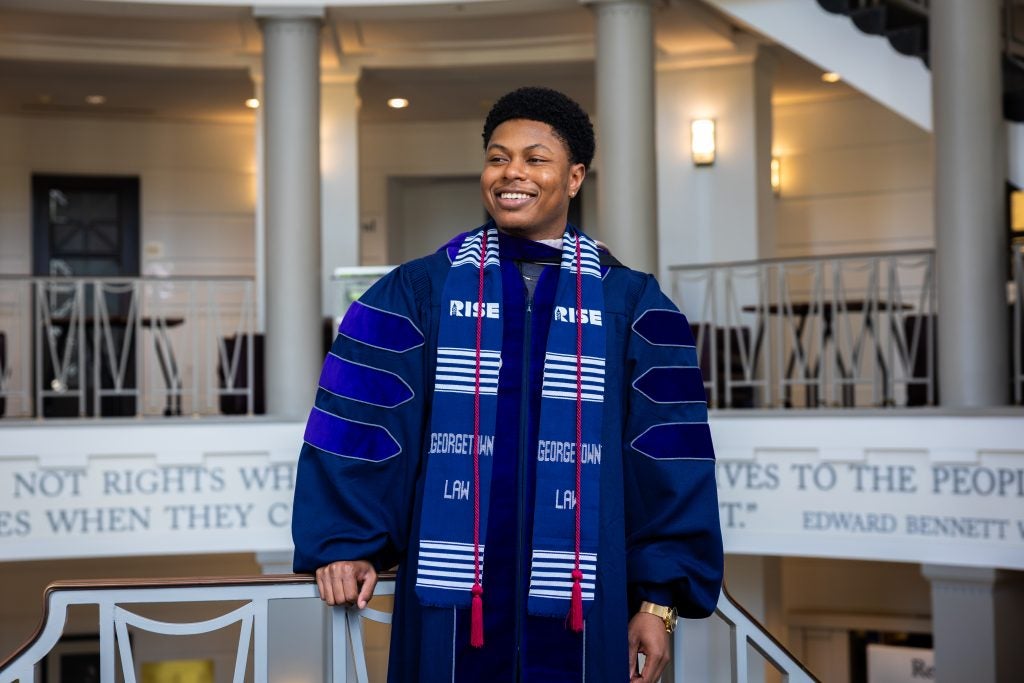 A young man smiles while wearing a purple graduation robe