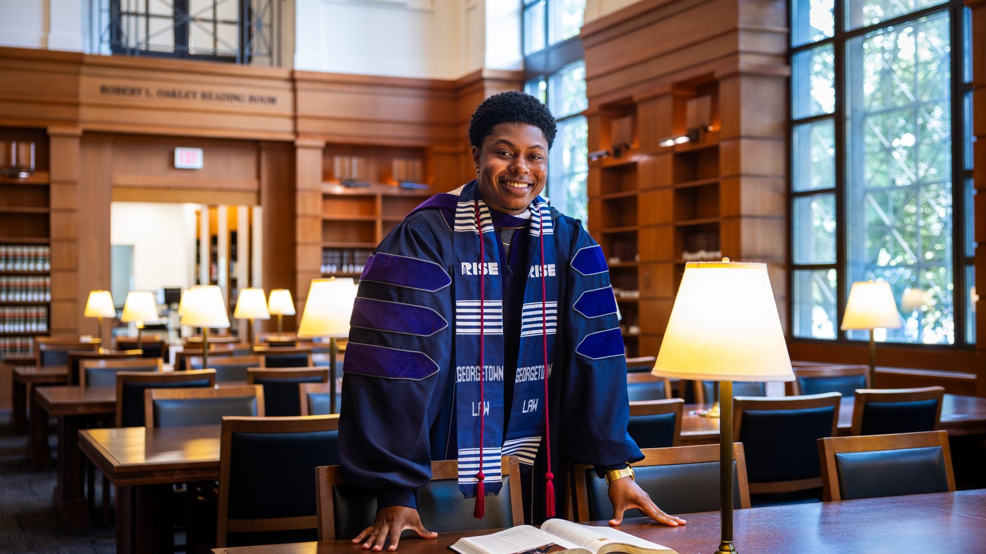A man in a purple graduation gown stands in a library
