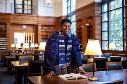 A man in a purple graduation gown stands in a library