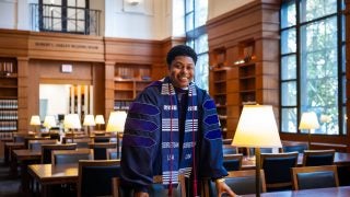 A man in a purple graduation gown stands in a library