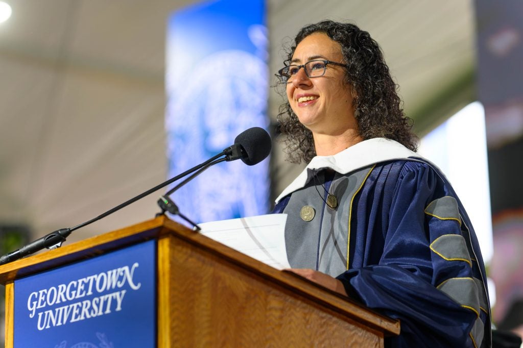 Woman with glasses smiles while speaking at podium