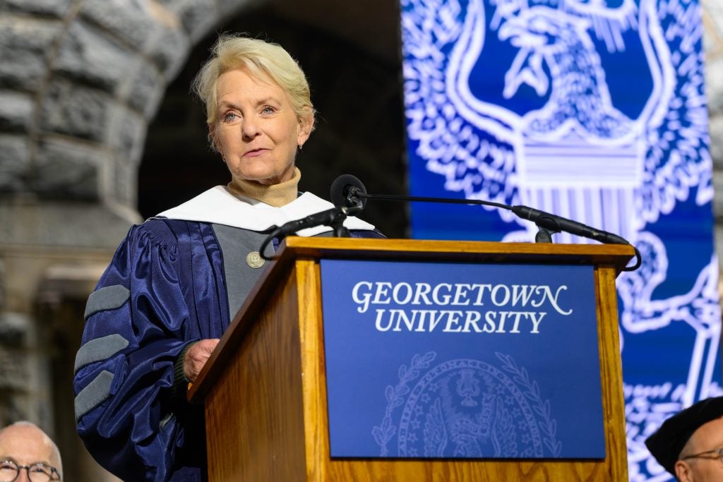 Older Caucasian woman speaks at a podium in commencement robe
