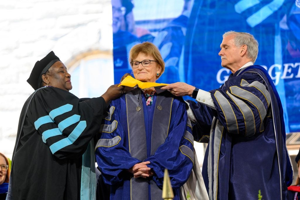 Black woman and Caucasian man put on doctoral hood on an older Caucasian woman in grad gown