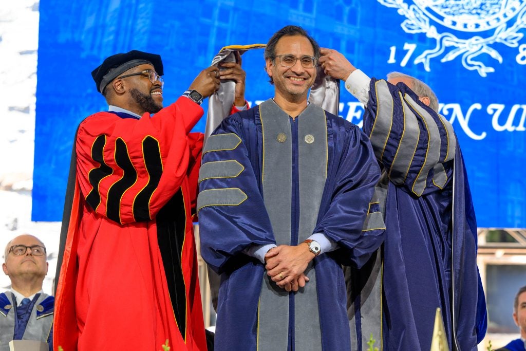 Two men put a doctoral hood on a man in grad gown while smiling