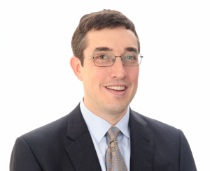 A headshot of a man wearing glasses and a suit and tie