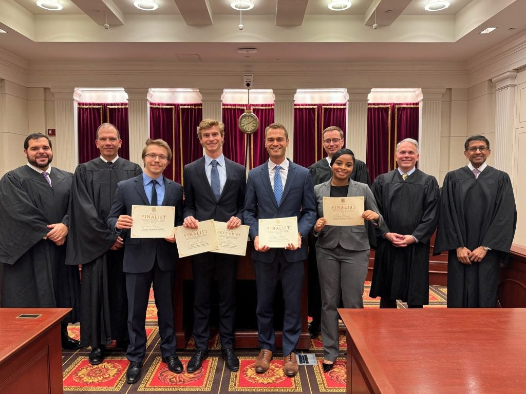 Students in legal robes holding up awards inside a moot court room