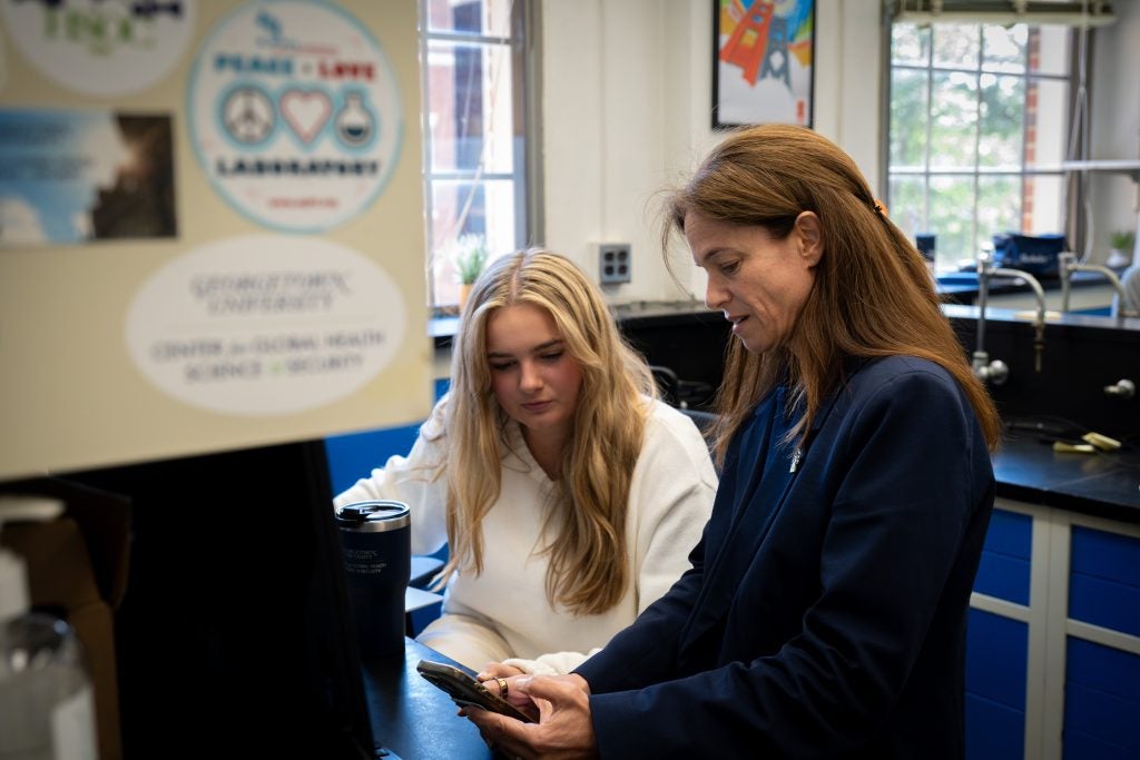 Woman in blue suit shows a student something on her phone