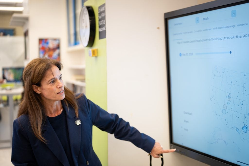 Woman in a blue suit points to a TV screen