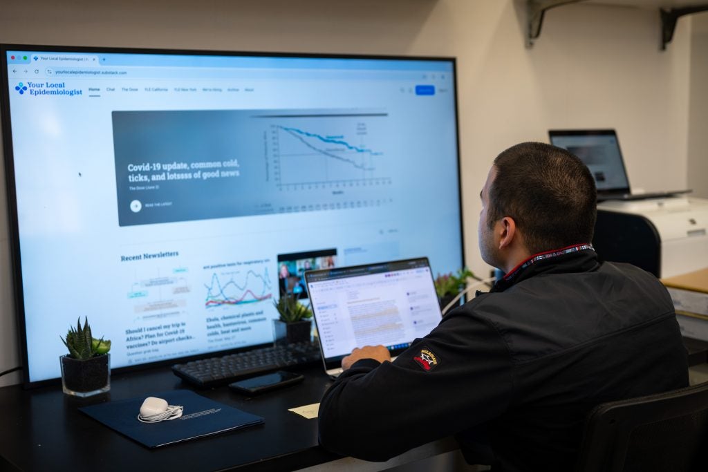 Young man looks up at a large screen while working on a laptop
