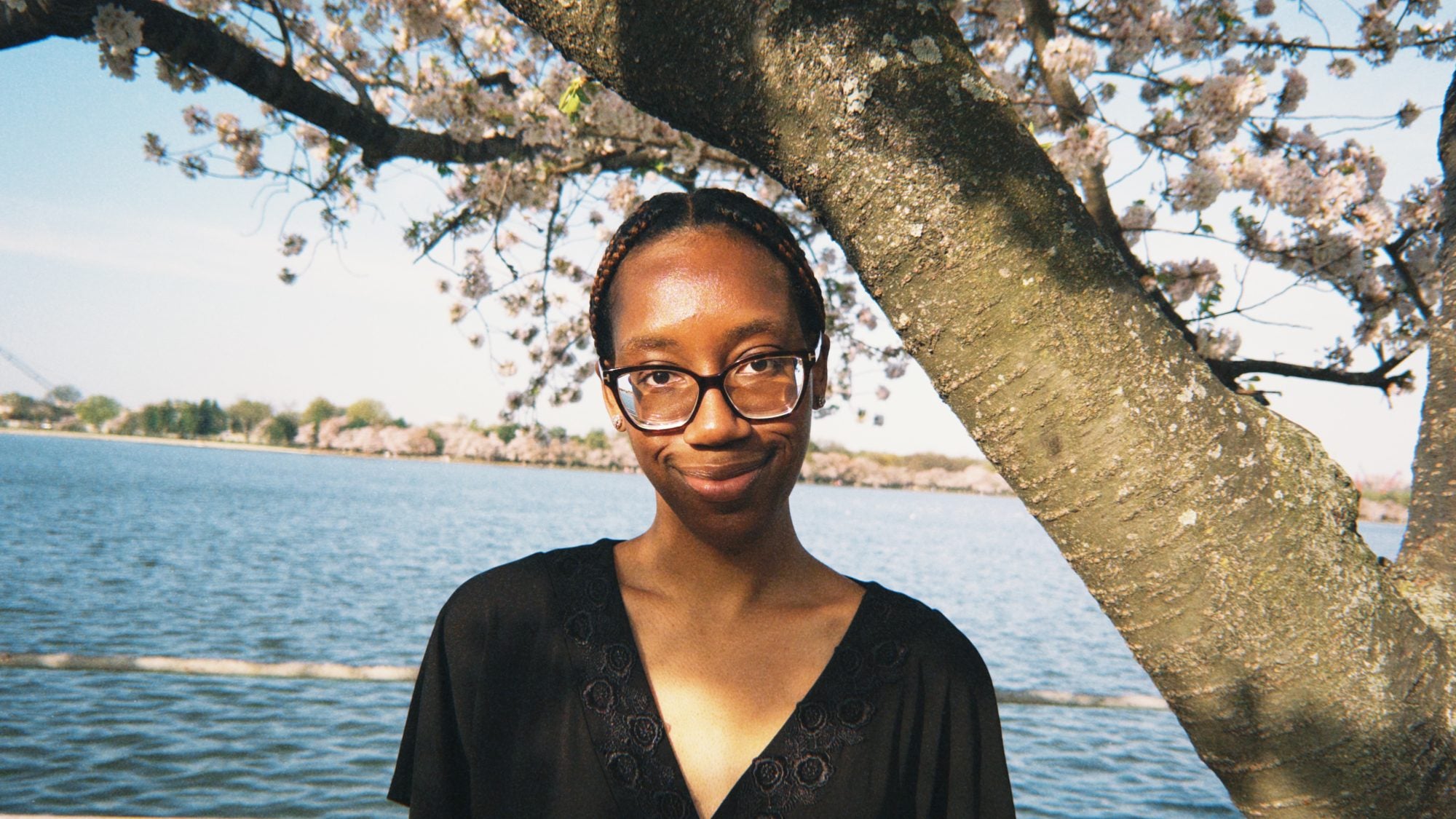 Young Black woman smiling in front of cherry blossoms