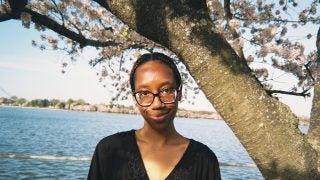 Young Black woman smiling in front of cherry blossoms