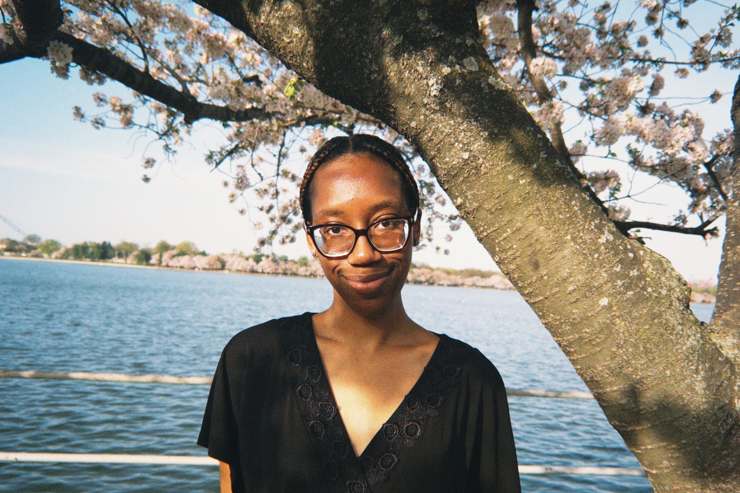 Young Black woman smiling in front of cherry blossoms