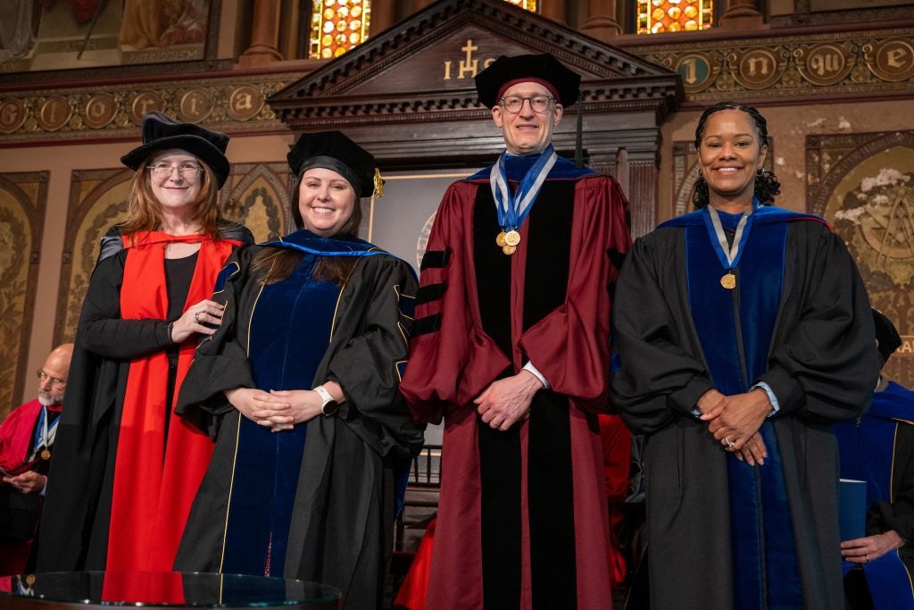 Four people in doctoral robes on stage