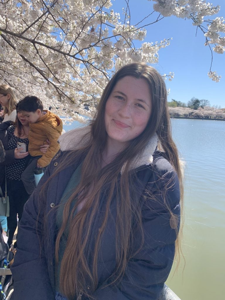 Young woman standing by cherry blossom trees